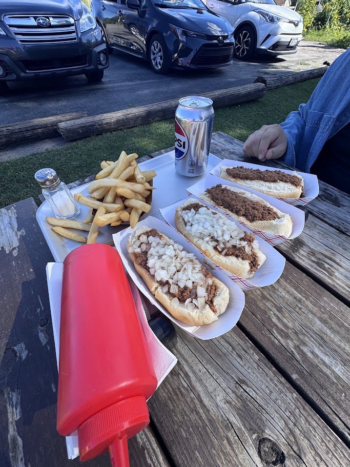 Outdoor picnic tables beside a roadside hot dog stand.